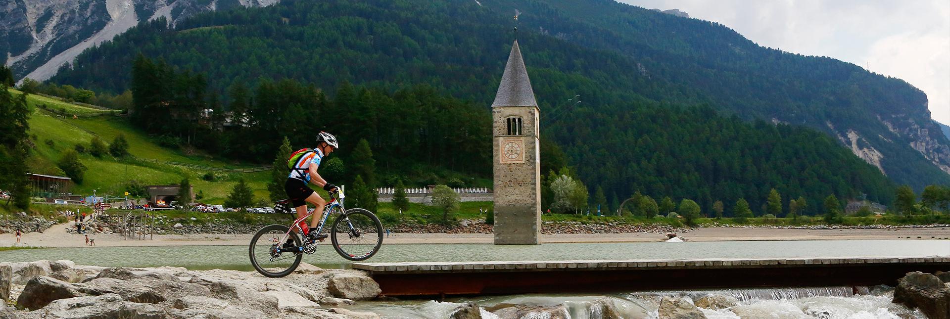 Un ciclista passa accanto al campanile sommerso nel Lago di Resia